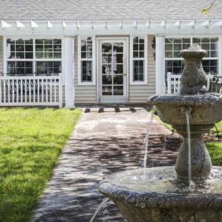 A peaceful garden with a stone fountain leading to a charming house.