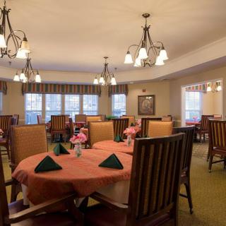 A well-decorated dining room with multiple tables set for a meal, featuring chandeliers and floral centerpieces.