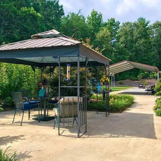 A peaceful outdoor area featuring a gazebo with chairs, surrounded by lush greenery and trees.