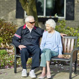 An elderly couple sitting together on a park bench enjoying the outdoors.