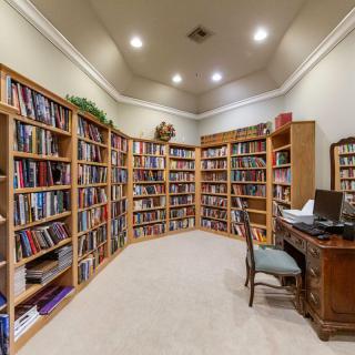 A cozy library with bookshelves lined with numerous books and a wooden desk with an ornate chair in the center.
