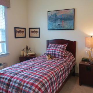 A cozy bedroom with a single bed featuring plaid bedding, decorated with wall art and a bedside lamp.
