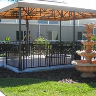 An outdoor gazebo with a metal railing and a decorative fountain nearby, set in a landscaped garden.