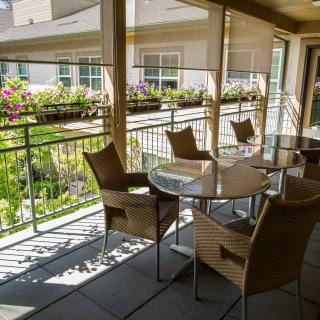 A sunlit patio with wicker chairs and a glass table overlooking a garden.