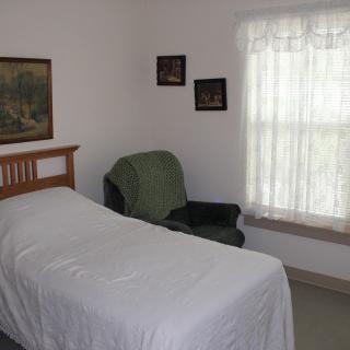 A minimalist bedroom with a single bed, an armchair, and a window with sheer curtains.