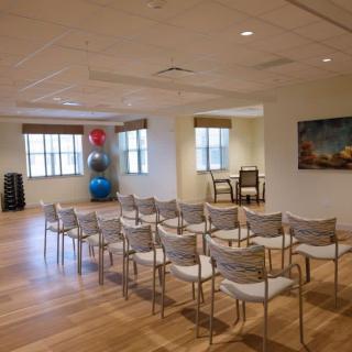 A versatile meeting room with neatly arranged chairs, wooden flooring, and exercise equipment in the corner.