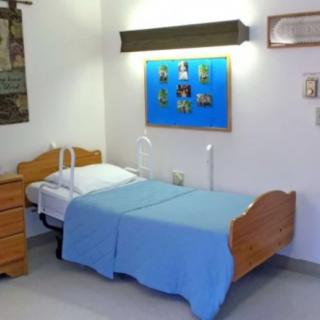 A neatly made bed with blue bedding in a simple, well-lit room with minimal decor.