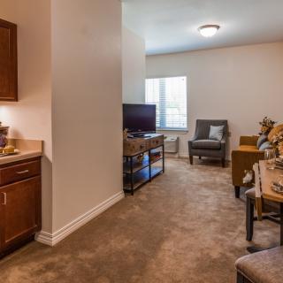 A cozy apartment interior with a small kitchen and living room featuring comfortable seating and a television.