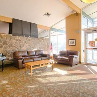 A cozy lobby with leather sofas and a coffee table, warmly illuminated by natural light streaming through large windows.