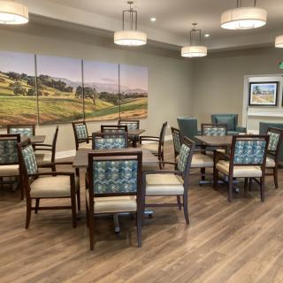A modern dining room with neatly arranged tables and chairs, featuring elegant lighting and wall art.