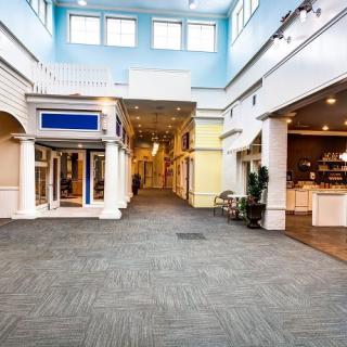 An empty shopping mall interior with storefronts and classical architectural features.