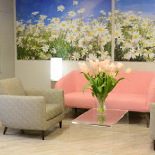 A cozy lounge area featuring a pink sofa, gray chairs, and a beautiful flower arrangement against a backdrop of floral artwork.