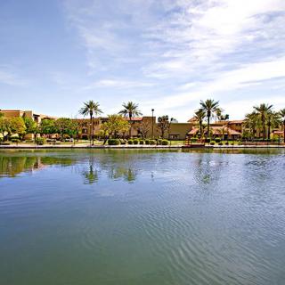 A serene lake with palm trees and resort buildings in the background under a clear sky.