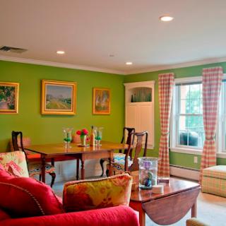 A vibrant living room featuring green walls and a cozy seating area, complemented by decorative paintings and a dining table.
