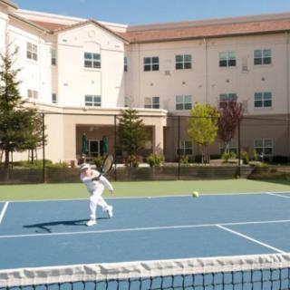 A person playing tennis on an outdoor court in front of a building.