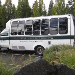 A white minibus parked outdoors surrounded by greenery.