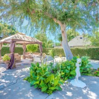 A serene garden with a gazebo, surrounded by lush greenery and a sculpture under a sunny sky.