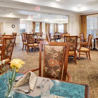 A spacious dining room with elegantly set tables and chairs, featuring floral decorations.