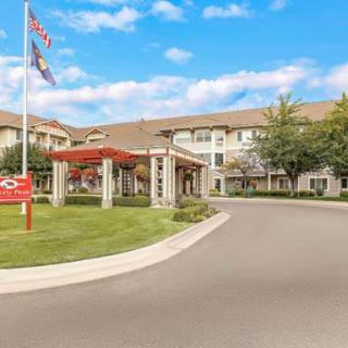 A well-maintained building with a welcoming entrance, surrounded by manicured landscaping and adorned with flags, under a blue sky with scattered clouds.