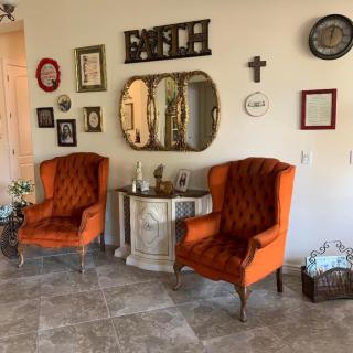 A cozy vintage living room with orange armchairs, a decorative wall mirror, and various wall art.