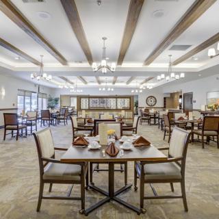 A spacious and elegantly decorated dining room with tables and chairs arranged neatly, featuring chandeliers and wooden ceiling beams.