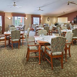 An empty dining room featuring neatly arranged tables and chairs with a carpeted floor and ceiling fans.