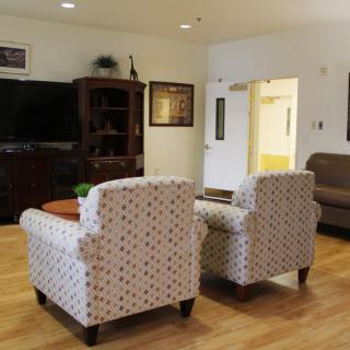 A cozy living room featuring patterned armchairs, a TV, wooden cabinet, and a comfortable sofa on a wood floor.