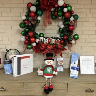 A festive Christmas-themed display featuring a wreath made of red, green, and white balloons, with a snowman figure and various decor items on the shelf below.