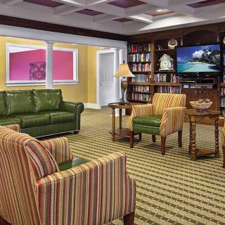A cozy living room with a green couch, striped chairs, bookshelves, and a television.
