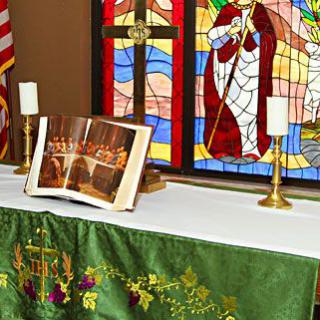 A church altar with an open Bible, candles, and a stained glass window in the background.
