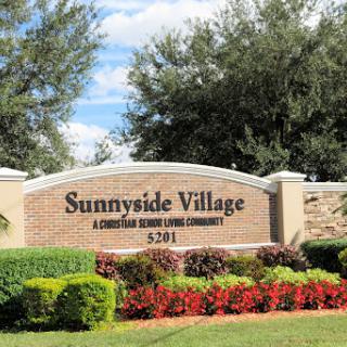 Entrance sign of Sunnyside Village, a living community surrounded by beautiful landscaping.