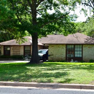 A suburban house with a tree in the front yard and a car parked in the driveway.