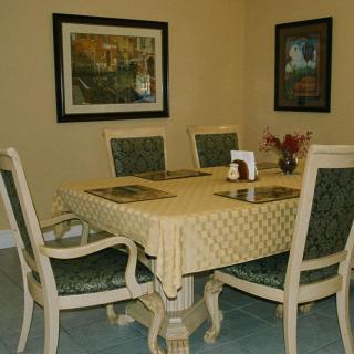 A cozy dining room setup with a table and chairs, adorned with a patterned tablecloth and surrounded by framed paintings on the walls.