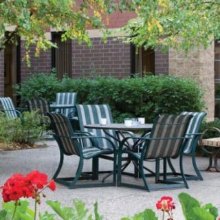 An outdoor patio area with metal chairs and a table surrounded by lush greenery.