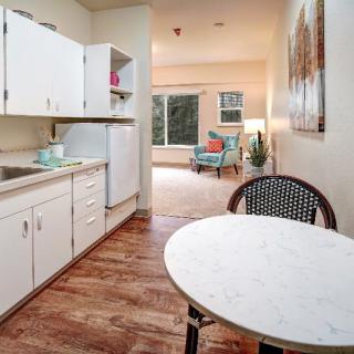 A small kitchen with white cabinets opens up to a cozy living area featuring wooden floors and modern decor.