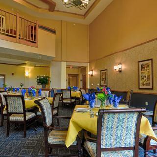 An elegant dining room with neatly arranged tables adorned with yellow tablecloths and blue glasses.