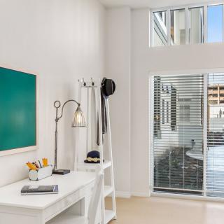 A modern and minimalist office space with a desk, lamp, artwork, and large window blinds.