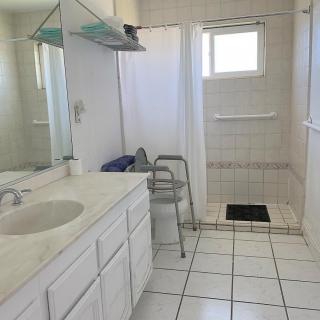 A clean, white-tiled bathroom with a sink, mirror, and accessible shower area.