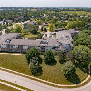Aerial view of a large building surrounded by trees and roads in a suburban area.