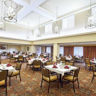 A spacious and elegant dining room with multiple set tables and chandeliers overhead.