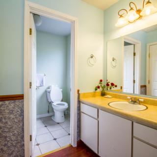 A bright bathroom featuring a yellow countertop, white cabinets, and a well-lit mirror.