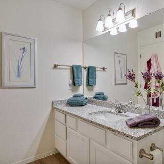A modern bathroom with a large mirror, decorative flowers, and teal towels neatly arranged.