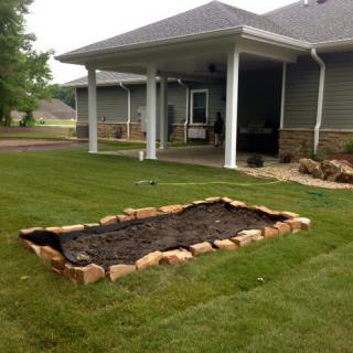 A backyard garden with a stone-bordered flower bed ready for planting.