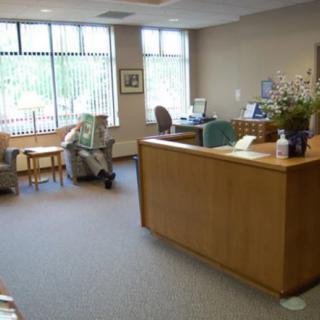 A reception area with a desk and a person sitting in the waiting area reading a newspaper.