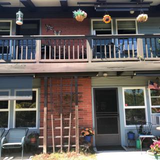 A two-story house with a balcony, hanging plants, and outdoor seating in the garden.