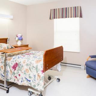 A serene hospital room featuring a patient bed with floral bedding, a comfortable chair, and a bright window.