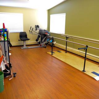 A rehabilitation room equipped with parallel bars and various exercise equipment.