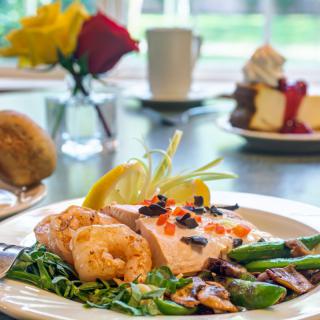 A gourmet meal featuring salmon with vegetables and a dessert in the background.