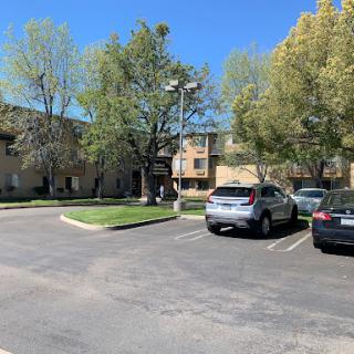 A sunny day in an apartment complex parking lot, featuring several parked cars and lush trees.