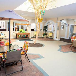 A bright indoor seating area with tables, chairs, and plants under a skylight.
